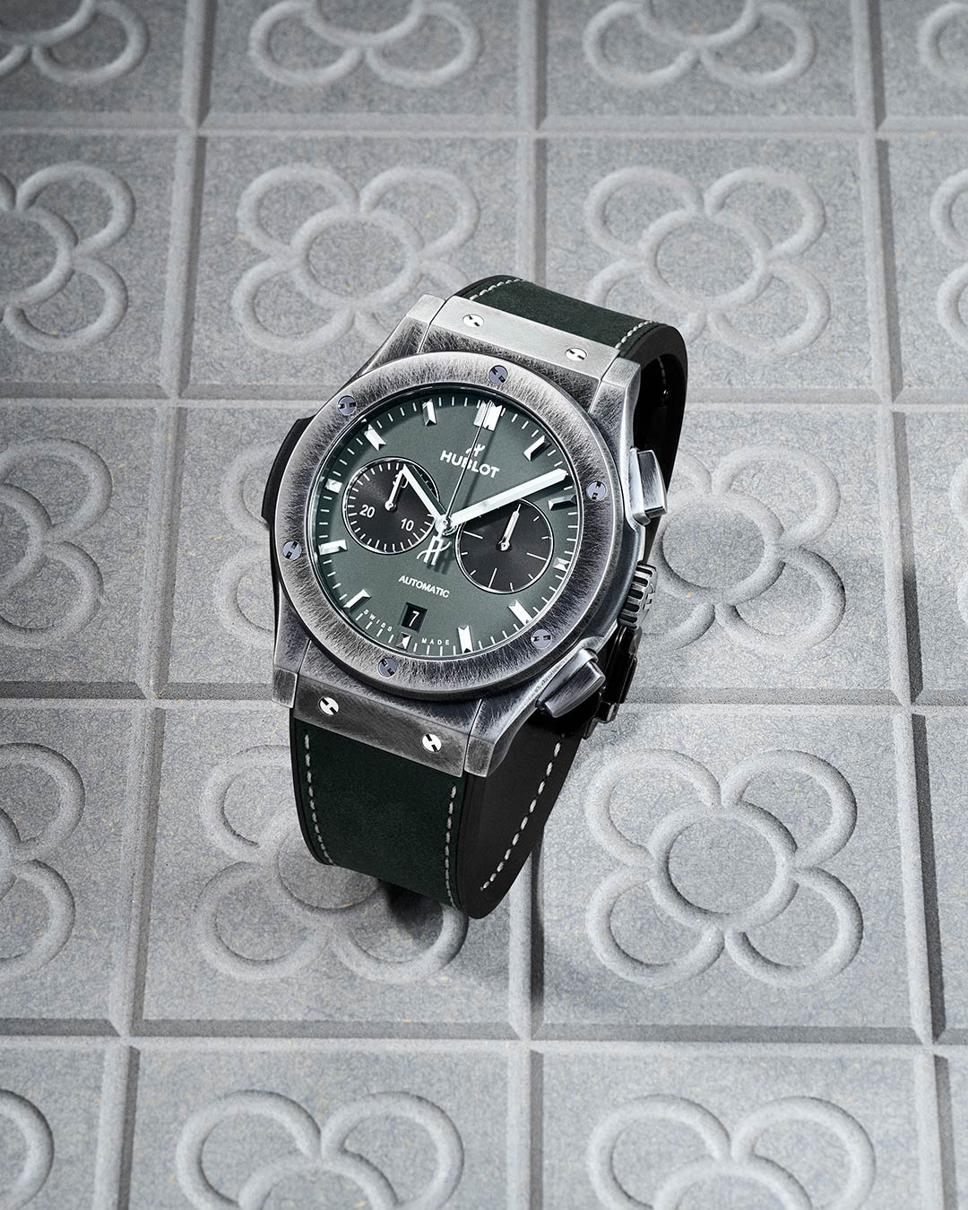 Reloj verde con correa de caucho y caja de titanio envejecida sobre fondo de baldosa de Barcelona